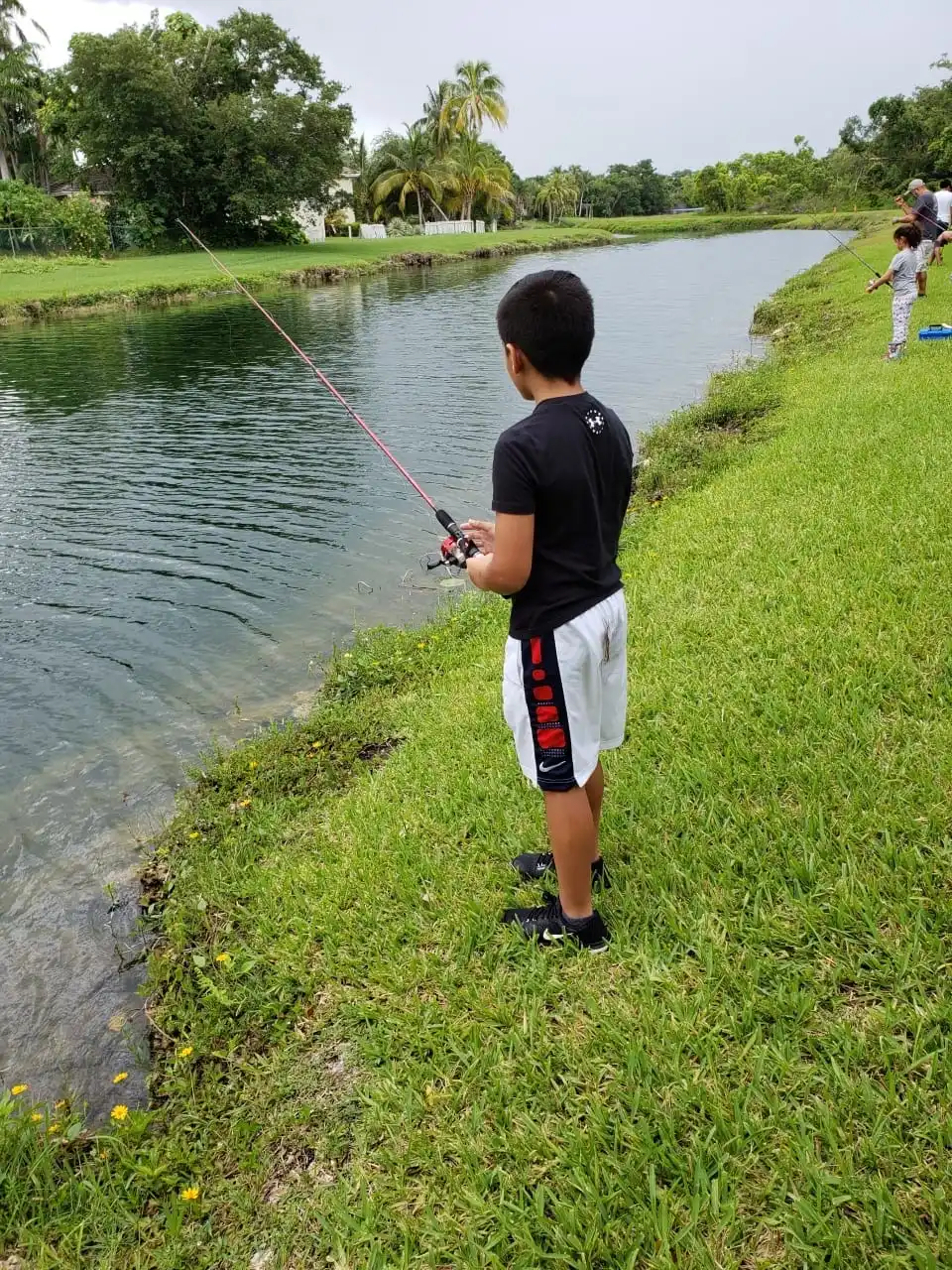 A boy standing at the edge of a canal, back to the camera, watching the water