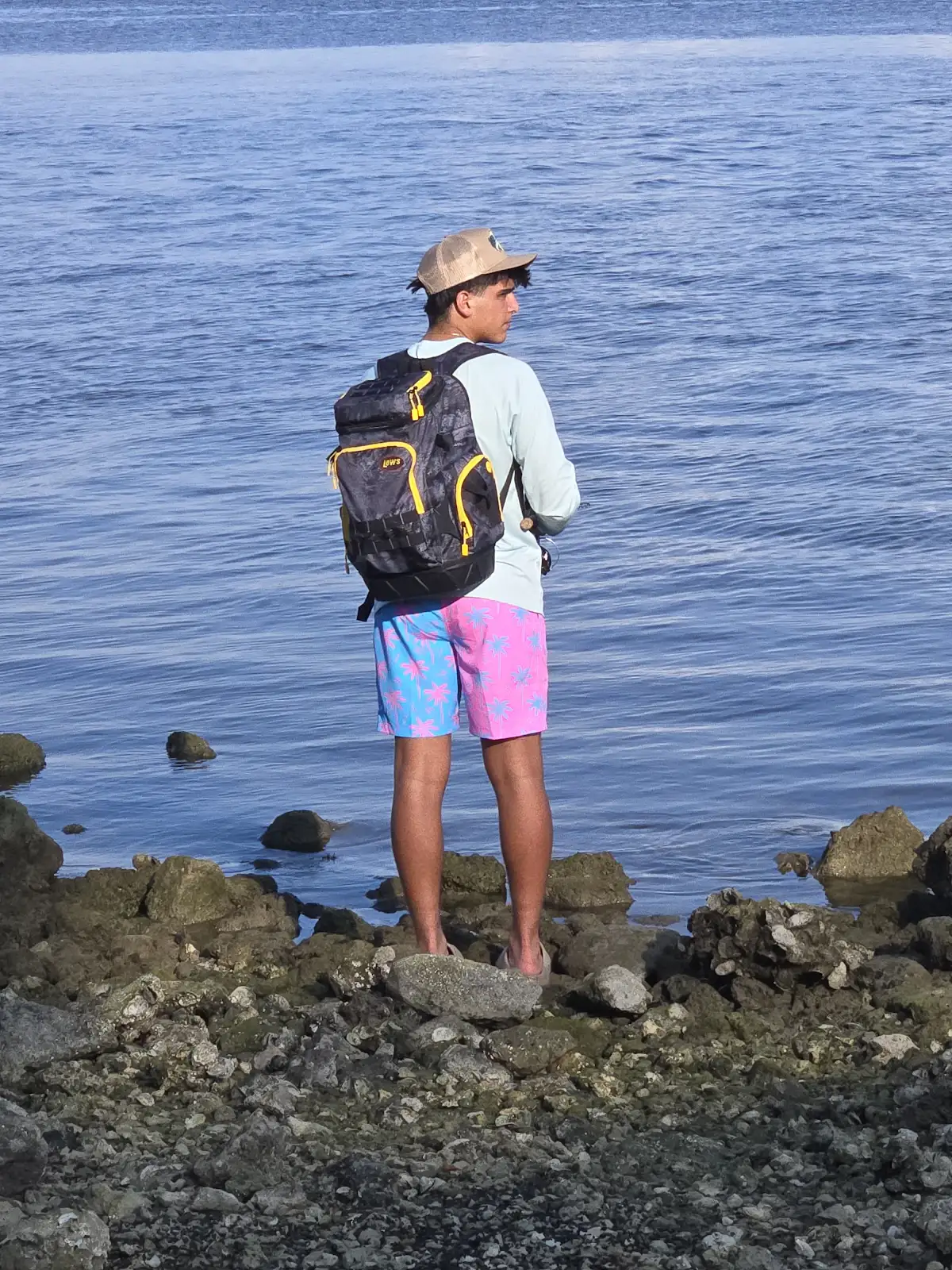 A teenager standing on rocks at the water's edge, scanning the sea