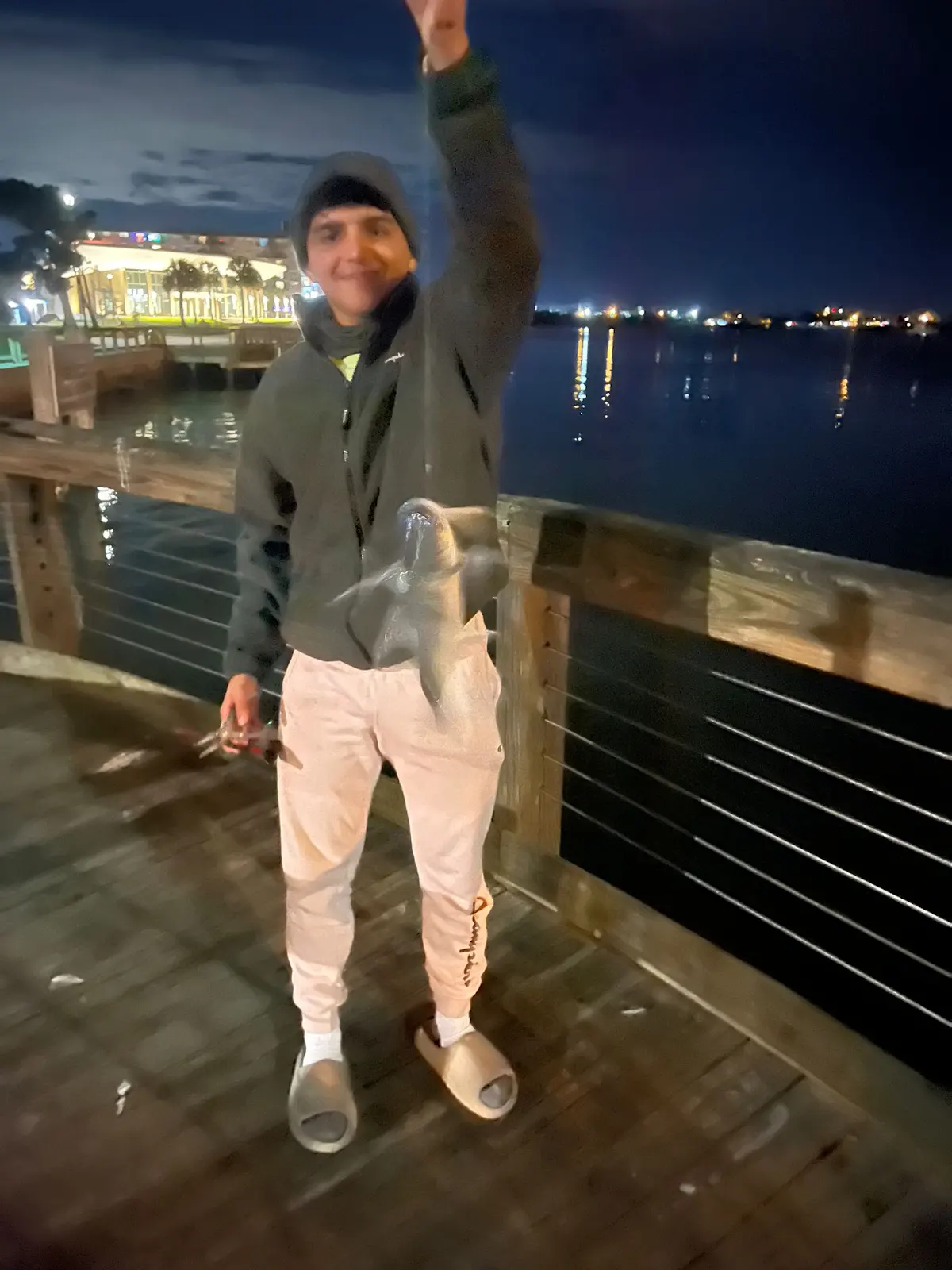 A blurred night photo on a dock, holding up a catch under string lights