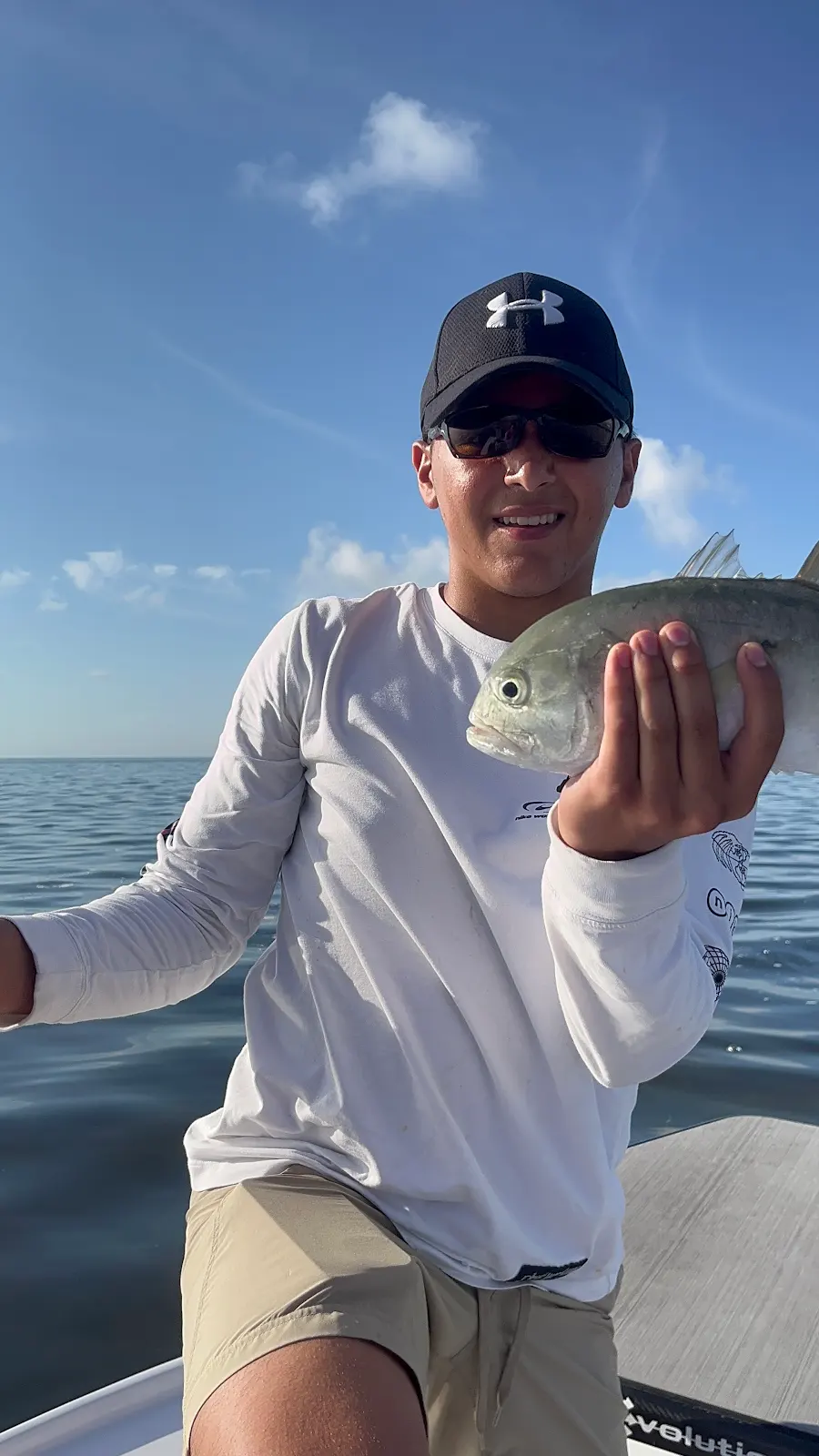 A teenager on a boat offshore holding a small jack crevalle
