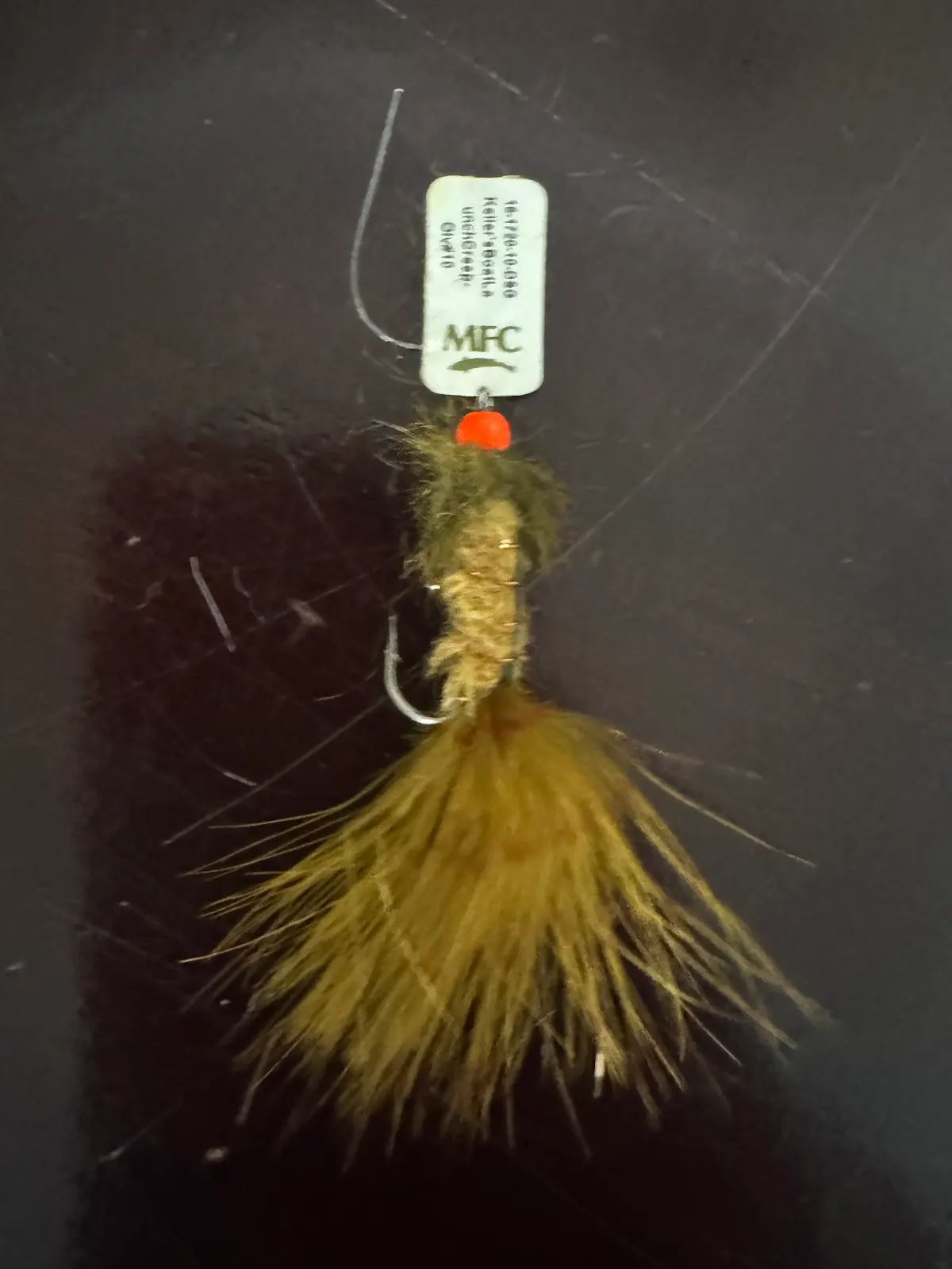 Close-up of a hand-tied olive fly with an MFC tag, hook visible